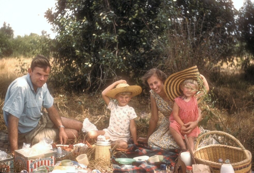 A mother and father take their young family for a picnic in a meadow. Moments like these show the love between a family and are helpful when thinking about how to write an obituary.