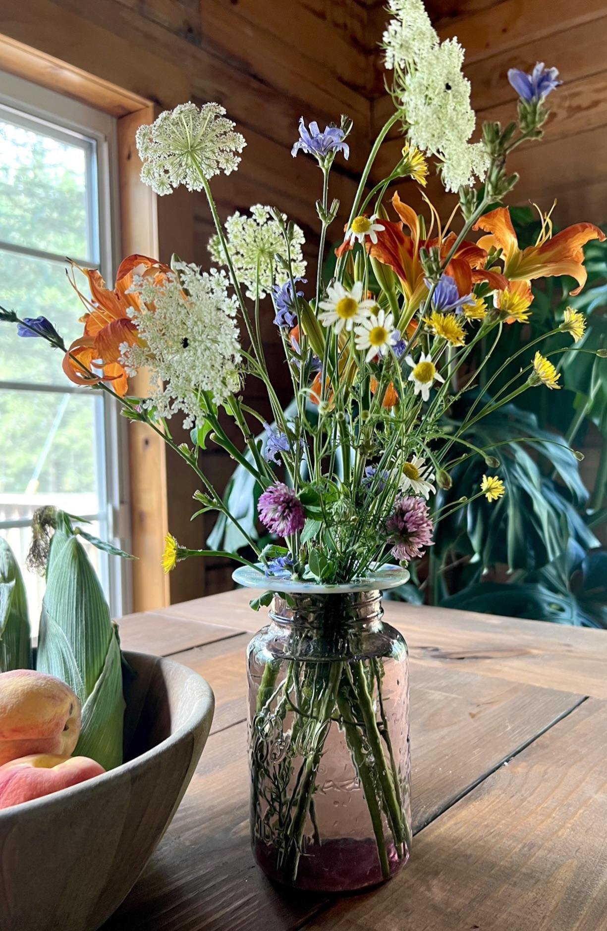  A small bouquet of colorful wildflowers rests in a mason jar on a wooden table to memorialize a parent. 
