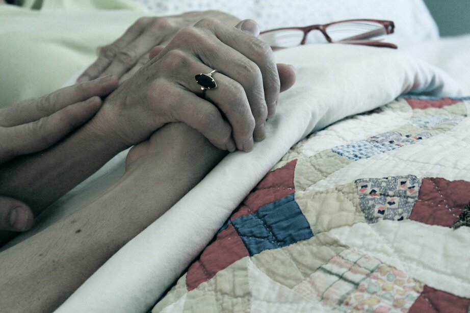  Two hands intertwine with love at the bedside of someone in the process of dying. 