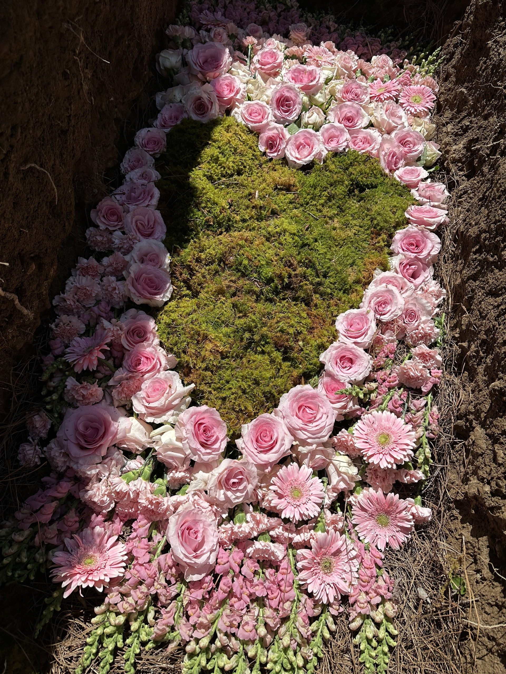 Pink flowers rest on top of a bed of moss to decorate the bottom of grave at Larkspur.