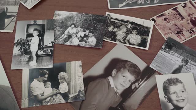 Black and white photos of children and family members displayed on a wood table. Old family photos helpful when thinking about how to write an obituary.